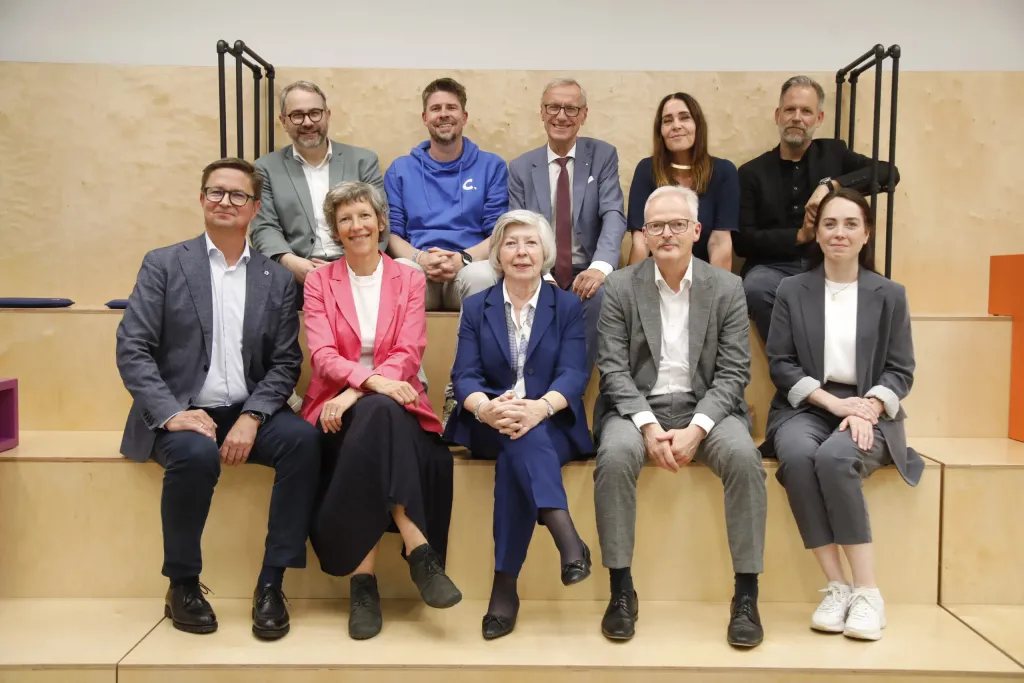 Gruppenfoto: elf Personen sitzen auf einer Holztribüne