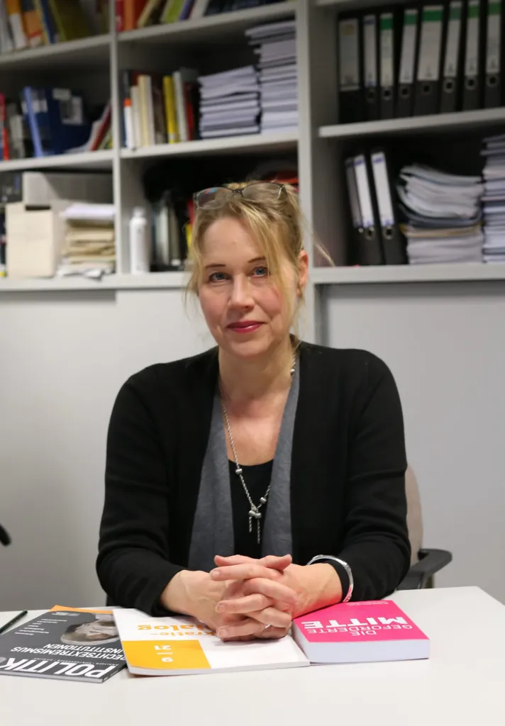Porträt von Beate Küpper an einem Schreibtisch vor Bücherregalen, vor ihr liegen Publikationen