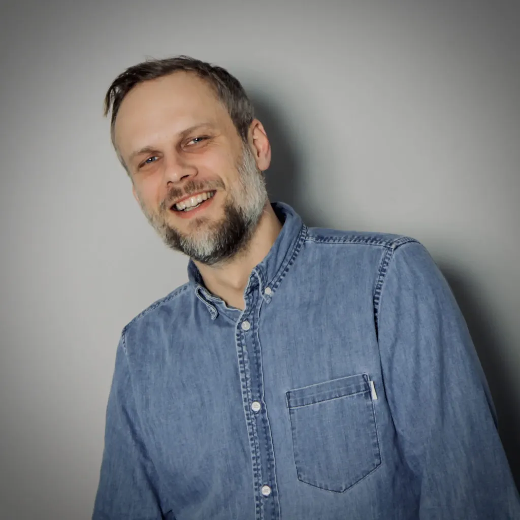 Porträt eines lächelnden Mannes mit Bart in blauem Jeanshemd